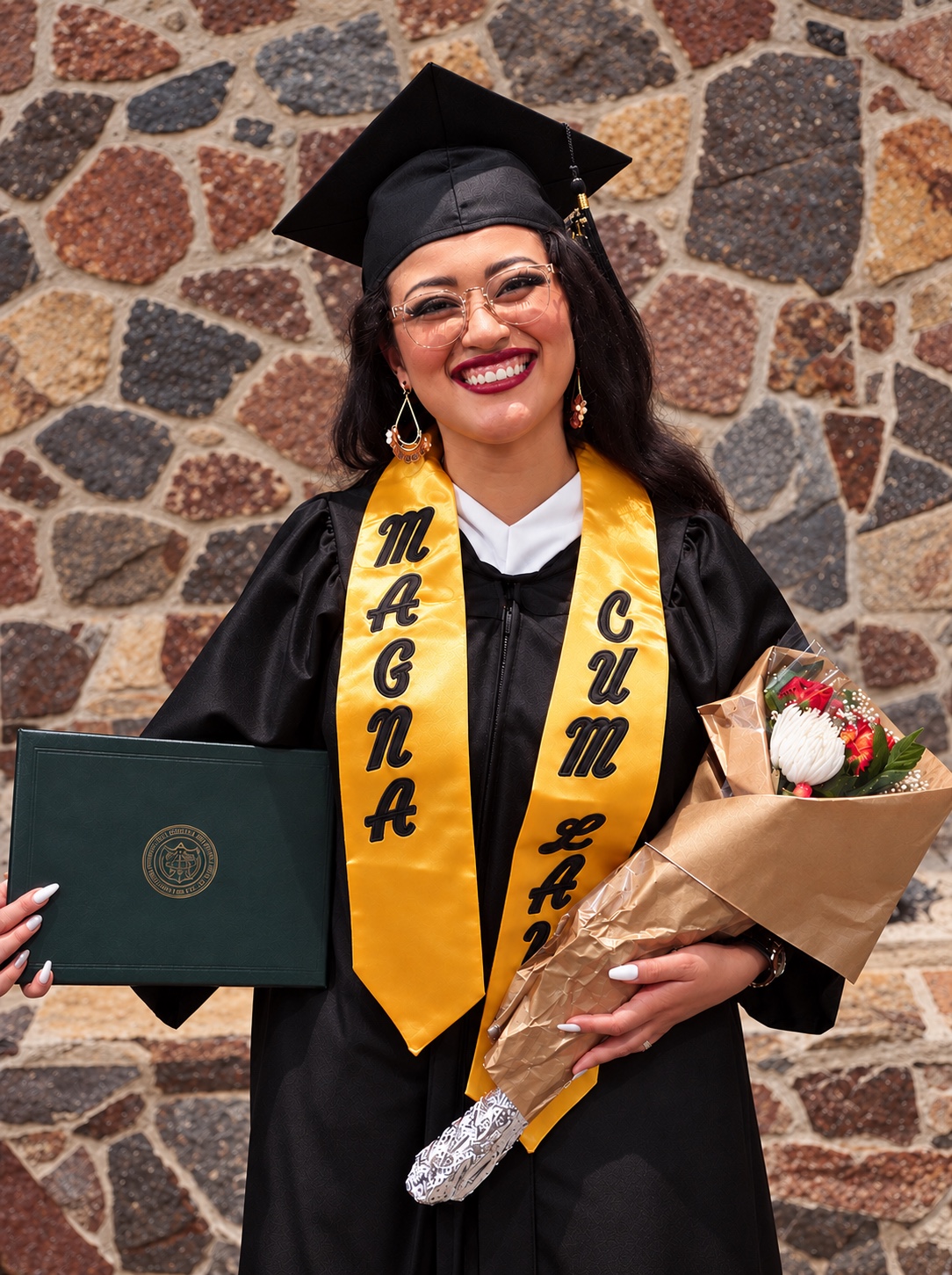 Lesliebeth Sánchez Sierra en su graduación, con toga, estola magna cum laude, diploma y flores