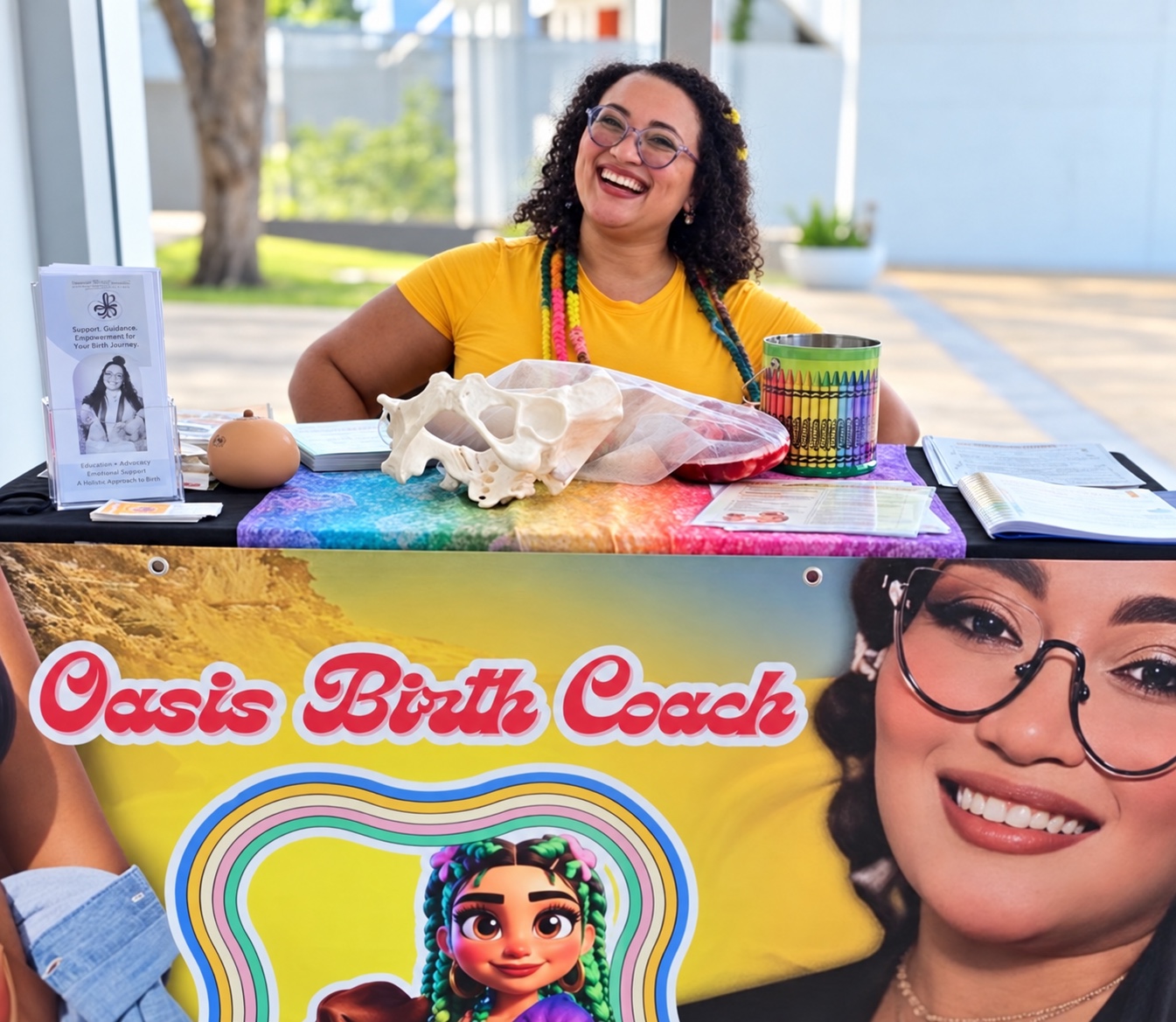 Lesliebeth en una mesa de Oasis Birth Coach con materiales de educación perinatal y el banner de su proyecto